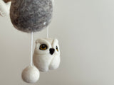 A felt owl baby mobile suspended from a string, featuring a soft woolen owl with fluffy texture and detailed wings. The neutral background allows the owl to be the main focus. Made of wool felt, this charming mobile promises endless fun for your little one.