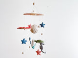 A sea life wool felt baby mobile hangs against a plain white background. It features a wooden frame from which various wool felt sea creatures are suspended by thin white threads. The colorful creatures include white scallops, blue dolphins, green sea turtles, grey seahorses, whales, and stingrays. Small white felt balls are interspersed, creating a serene and balanced design.