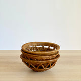 A stack of three small, round handmade Bali rattan baskets woven from ata grass. They feature a decorative open-weave pattern and are nested on a light wood table against a white wall, presented as unique home decor handmade in Bali.