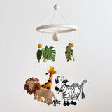 A felt baby mobile, featuring a jungle safari theme, is suspended against a white background. The mobile consists of three main figures: a zebra, a giraffe, and an elephant, each distinct in color and shape. The zebra is black and white, the giraffe brown and orange, and the elephant gray. They hang from a circular frame attached to the ceiling by a string.