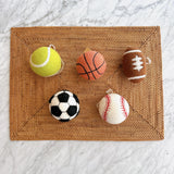 A handmade wool felt basketball ornament, a unique Christmas decoration, is arranged on a textured, light brown woven mat against a bright marble backdrop. The orange felt basketball features black seam lines and is topped with a white cotton string, perfect for any sports-themed Christmas tree.