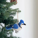 A needle-felted bluejay ornament, part of a Felt Bird Ornaments Set, hangs gracefully from a Christmas tree. This handcrafted wool felt bluejay features vibrant blue on its head, wings, and tail, with a white and gray body, small dark eyes, and a black beak. Dark wire legs and a jute string complete this charming Christmas tree ornament.
