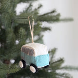 A retro wool felt blue camper van ornament hangs on a green Christmas tree branch. The unique Christmas ornament features a two-tone design with a light blue lower half and a white upper section. Small grey windows and round black and white wheels add charming details to the vehicle. A jute string is attached to the top for easy hanging.