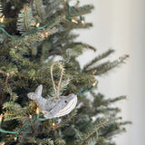 One of the felt whale Christmas ornaments hangs gracefully on a Christmas tree adorned with twinkling lights. This handcrafted gray felt whale features a rounded body, a tail, and a white underbelly, with a jute string attached for hanging. The festive scene showcases the unique Christmas tree ornament amidst lush green needles and soft glowing lights, creating a cozy holiday atmosphere.