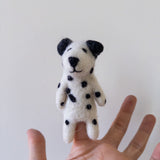 A handmade felt Dalmatian dog finger puppet is presented by a hand against a plain white backdrop. This charming felt finger puppet features a white body with distinct black spots, black ears, and a black nose, showcasing its meticulous handcrafted design.