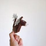 A handmade gray wool felt donkey finger puppet is playfully displayed on a finger against a plain white backdrop. This charming needle felted finger puppet features a gray body, a fluffy gray mane, and a tail. Its 3D design, small ears, and simple stitched facial features make it a delightful handcrafted felt kids toy, perfect for storytelling.