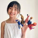 A young girl holds up a set of five colorful felt finger puppets shaped like birds, resting on her hands. The background is a simple white wall, allowing the main subject—the finger puppet set—to stand out. Each bird-shaped finger puppet boasts intricate details and vibrant colors, crafted from high-quality wool felt.