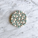 A set of four felt light blue round coasters rests on a white marble surface with subtle gray veining. Each handcrafted felt coaster is made from small, hand-stitched balls of 100% organic lamb wool in varying shades of light blue. Ethically handmade by Nepalese female artisans, these unique wool felt coasters offer a calm, minimalist aesthetic.