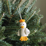 A felt duck ornament hangs from a green Christmas tree branch. This cheerful duck ornament features a white felt body, orange feet, a yellow beak, and a small tuft of hair, suspended by a white string.