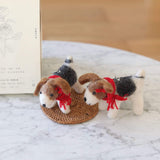 Two needle felted Jack Russell dog Christmas ornaments are presented on a light marble surface, with one positioned slightly behind the other on a small, round woven mat. Each handmade ornament is meticulously needle felted and hand-stitched, showcasing the Jack Russell's distinctive white, brown, and black markings. A red cotton string is tied around each dog's neck, adding a festive touch.