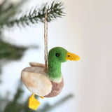 A wool felt Mallard Duck ornament hangs on a Christmas tree, featuring a vibrant green head, yellow bill, and chestnut chest. Handcrafted with needle-felted details, this unique Christmas ornament has distinctive blue wing patches, a light beige and brown body, and yellow feet. A jute string is attached for easy hanging.