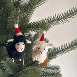 Two sheep ornaments with Santa hats hanging on a Christmas tree branch.