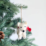 A fluffy white felt polar bear ornament hangs on a Christmas tree. This charming polar bear ornament wears a vibrant red scarf, with black bead eyes and nose. A jute string is attached for easy hanging.