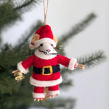 A handmade wool felt Santa mouse ornament hangs from a green Christmas tree branch, evoking a festive and joyful mood. The charming felt mouse wears a red Santa suit with white trim, a black belt with a gold buckle, and a red Santa hat. It features a white face, pink nose, black whiskers, and holds a small gold bell.