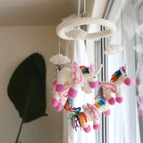 A felt unicorn baby mobile hangs from a ceiling hook, featuring three colorful unicorns with unique patterns on their manes. Each unicorn is attached to the mobile by strings, allowing them to spin freely. The product is made of 100% New Zealand wool felt and features a simple, eco-friendly design.