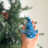 A unique blue felt whale shark finger puppet is held gently in a female hand. This handcrafted felt kids toy features distinctive white markings resembling a starry night sky, tiny black eyes, and a stitched smile.