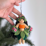 A Hula Girl Ornament is held by a female hand, prominently displayed against a lush green Christmas tree. This festive Christmas ornament features a light tan body, an orange top, and a dark green grass skirt. Adorned with a flower crown and flower bracelets, this charming ornament is ready to hang, bringing joyful, playful vibes to holiday decor.