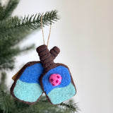 A vibrant wool felt pickleball ornament hangs from a Christmas tree. This handmade ornament is shaped like a pickleball paddle, crafted from wool felt in vibrant colors, and features a jute string for easy hanging.