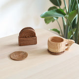 A set of brown rattan cup coasters with one coaster placed under a wooden cup, and a rectangular storage box in the background, all placed on a wooden surface.