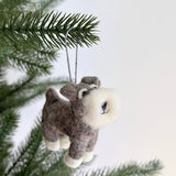 A felt Schnauzer dog ornament hangs from a vibrant green Christmas tree branch. The gray Schnauzer dog features a fluffy white beard and eyebrows, white paws, and a cute smile, suspended by a gray string.