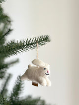 A playful white bunny wool felt ornament is shown, crafted from soft wool felt. It features long, floppy pink ears, a cute smiling face with black thread details, and a tiny pink nose. A jute string is attached for easy hanging, complemented by a brown tag.