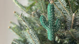 A handmade felt cactus ornaments by Ganapati Crafts hanging on a Christmas tree