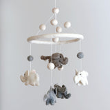 A hanging wool felt baby mobile, featuring a central circular frame suspended from which several soft, textured felt sea creatures are attached. A small elephant figure is positioned at the bottom center of the mobile.