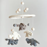 A felt baby mobile, featuring three animals - an elephant on the left, a monkey in the center, and a bird on the right - hangs from a string. The background is white, showcasing the vibrant colors of the wool felt animals.
