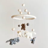A felt baby mobile, featuring a large round base with smaller circles attached, three felt animals - an elephant, horse, and bird - suspended from the base, and two felt balls. The mobile is made of wool felt and has a calm, playful mood, suggesting a peaceful environment for a baby.