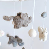 A felt baby mobile, featuring a small elephant figure, hangs from a string in a cozy nursery setting. The mobile's design elements are simple yet charming, with the elephant figure being the central focus. Made from 100% wool felt, this handmade mobile adds a touch of warmth and comfort to any baby's sleeping space.