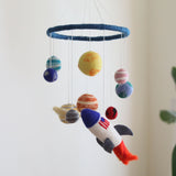 A colorful wool felt baby mobile, featuring planets and a spaceship, hangs from the ceiling. The soft, vibrant wool creates a whimsical space theme, with differently sized planets adding visual interest. Made of high-quality wool felt, this unique nursery decoration is both educational and entertaining for your little one.