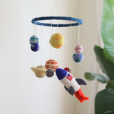 A colorful wool felt baby mobile, resembling the solar system, hangs from a string, featuring planets and a spaceship crafted from soft, vibrant wool felt. The mobile is designed for a nursery or crib, adding a touch of magic to a little one's room.