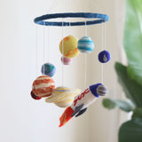 A colorful wool felt baby mobile, featuring planets and a spaceship, hangs from the ceiling, showcasing its playful and intricate design.