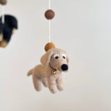 A cream-colored felt dachshund dog, part of a charming felt baby mobile, is captured in a close-up against a soft white background. This handmade dog features distinctive black felt eyes and a nose, highlighting its endearing design. A white felt frame is visible, with a second dachshund partially seen in the blurred background.