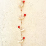 A charming felt shrimp garland hangs vertically against a textured, off-white wall. This whimsical garland features four light cream felt shrimp, each with subtle tan stripes and a vibrant red felt tail. They are evenly spaced along a thin, natural-toned twine, which is adorned with small, round felt balls in coordinating cream and light pink hues, adding a playful touch.