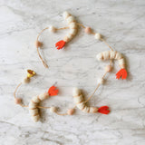 A felt shrimp garland rests on a white marble surface. This playful garland features four off-white felt shrimp with pink stripes and vibrant orange tails, alternating with small white and light pink felt balls strung along thin twine.