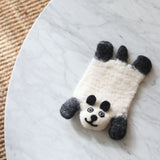 A handcrafted wool felt panda coaster, part of a set, is positioned on a round white marble table. This charming felt panda coaster features a creamy white body with distinctive black ears, limbs, and a smiling face, all meticulously needle-felted. The soft texture of the wool felt complements the marble's subtle gray veining, with a warm jute rug edge visible in the background.