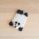 One handmade felt panda coaster rests on a light brown wooden surface, creating a calm and natural atmosphere. This wool felt coaster, approximately 7x4 inches, is crafted in the shape of a white panda with contrasting black ears and limbs. Its needled felted face features a sweet smile and round eyes, reflecting the ethical craftsmanship by Nepalese female artisans.