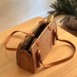 A handbag with a woven rattan exterior and leather handle rests on a wooden surface, possibly a table or shelf. The bag's design features a unique Batik lining, adjustable real leather handle, and secure snap closure. The overall mood of the image is casual and relaxed, with an emphasis on the handbag as the main subject.