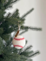 A needle-felted baseball ornament hangs from a lush green Christmas tree. This cheerful, 3-inch wool felt ornament is white with red stitches, replicating a real baseball design. It is suspended by a simple jute string, perfect for holiday decorations or for sports enthusiasts.
