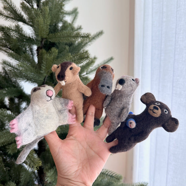 An Aussie animal felt finger puppet set of 5 is nestled against a soft, naturally lit background with a Christmas tree and sheer white curtains. This handcrafted, eco-friendly wool felt finger puppet set features a brown platypus finger puppet with a distinct duck-bill, along with four other Aussie animal finger puppets. They showcase hand-stitched details in varying shades of light grey, light brown, grey, and dark brown, perfect for imaginative play.