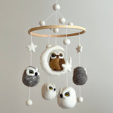 A whimsical wool felt baby mobile, featuring a wooden frame supporting a collection of colorful felt owls in various sizes, suspended from the ceiling by a string. The central brown owl has large eyes, while smaller unique white and gray owls surround it, creating a warm and playful atmosphere.