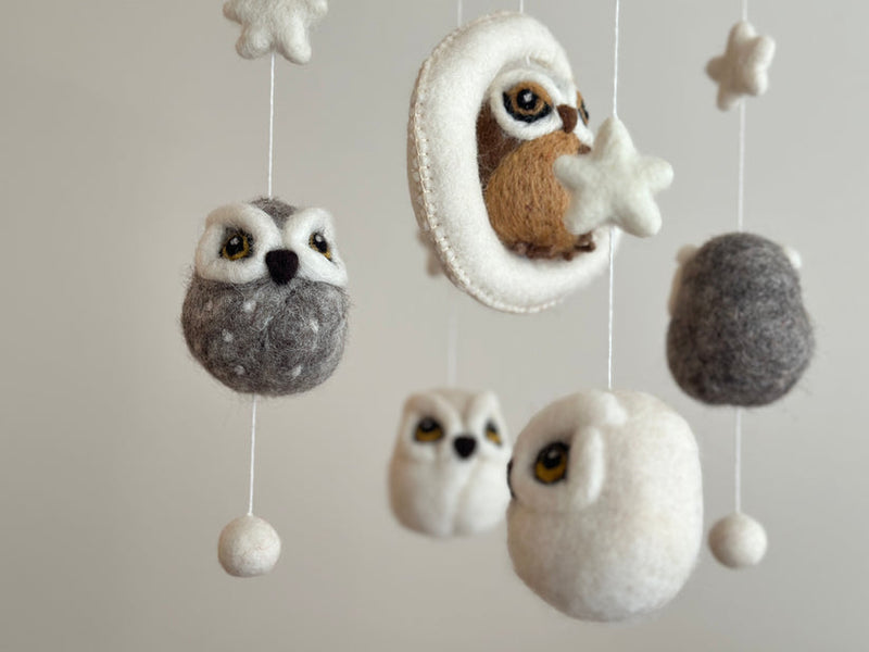 A wool felt baby mobile featuring an owl theme, suspended from a wooden frame with multiple owls of varying sizes and colors. Each owl has distinct features such as large eyes, small wings, and a round body, creating a playful and whimsical atmosphere in the child's room.