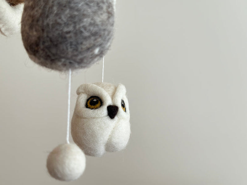 A felt owl baby mobile suspended from a string, featuring a soft woolen owl with fluffy texture and detailed wings. The neutral background allows the owl to be the main focus. Made of wool felt, this charming mobile promises endless fun for your little one.