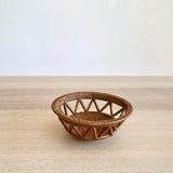 Front view of a single, small handmade Bali rattan basket woven from ata grass. The unique home decor piece, handmade in Bali, features a decorative open-weave and rests on a light wood table against a white wall.