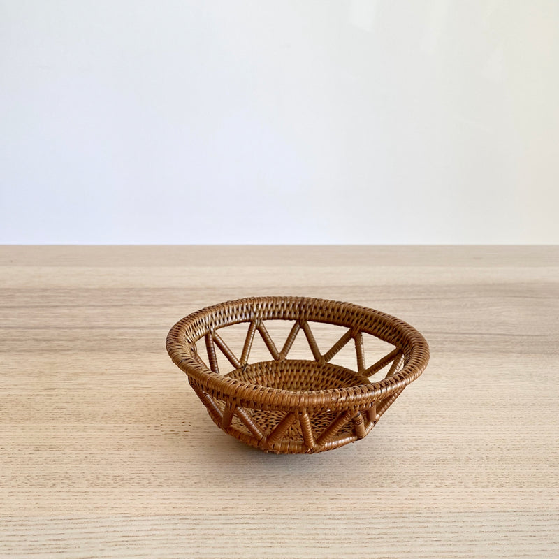 Front view of a single, small handmade Bali rattan basket woven from ata grass. The unique home decor piece, handmade in Bali, features a decorative open-weave and rests on a light wood table against a white wall.