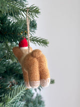 A charming needle felted Corgi Christmas ornament hangs on a festive Christmas tree. The detailed corgi ornament features short legs, white paws, and an adorable big butt, enhanced by intricate needle felting. It is adorned with a red and white Santa hat and suspended by a jute string.
