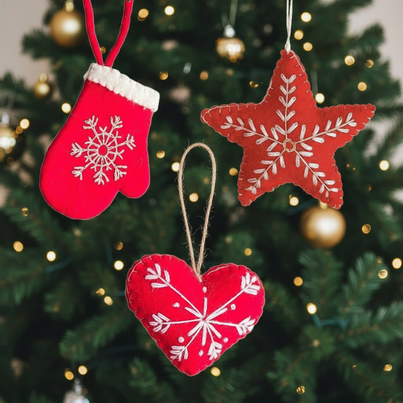 Red Christmas ornaments shaped like a star, heart, and mitten with white snowflake patterns on a white background.