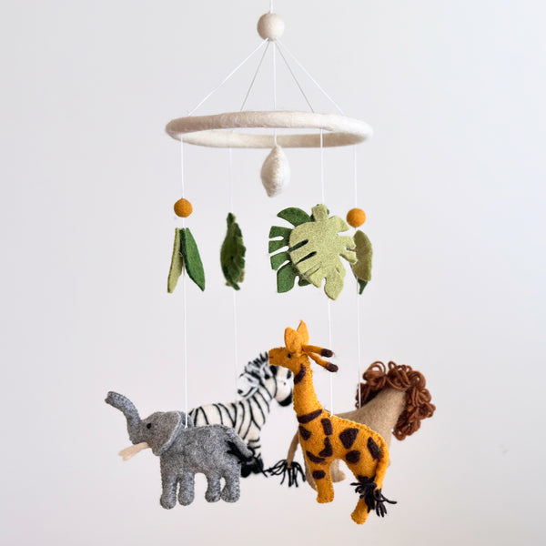 A vibrant wool felt baby mobile, titled 'Safari Jungle', hangs above a surface, featuring a collection of colorful felt animals including a zebra, giraffe, and elephant, along with decorative elements like leaves and feathers. The mobile's straightforward style showcases the Safari Jungle theme clearly.