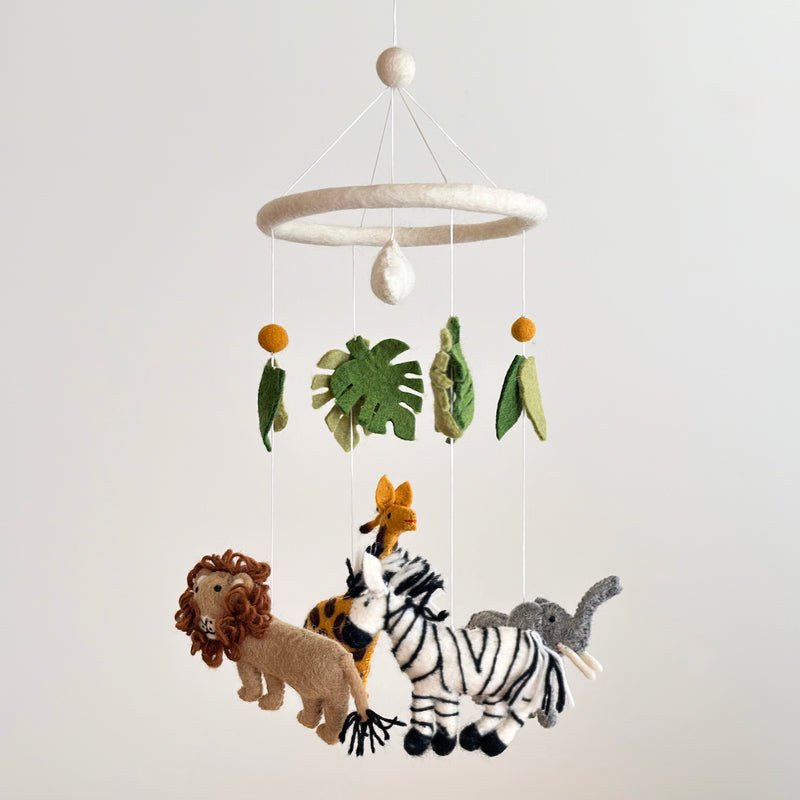 A felt baby mobile, suspended in mid-air against a white background, features a safari jungle theme. The mobile consists of a zebra, giraffe, and elephant, each depicted in a simplistic cartoonish style. The zebra is black and white, the giraffe brown and orange with long necks, and the elephant gray with large ears.